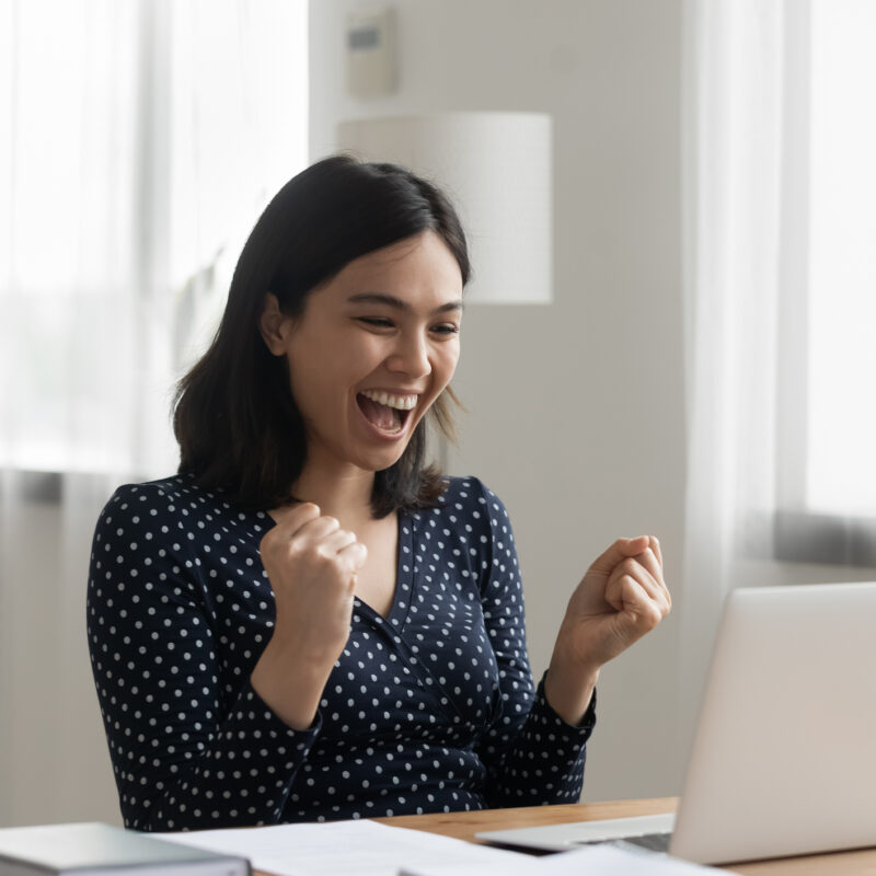 Excited young vietnamese woman look at laptop pc screen in delight receiving healthcare incentives and rewards